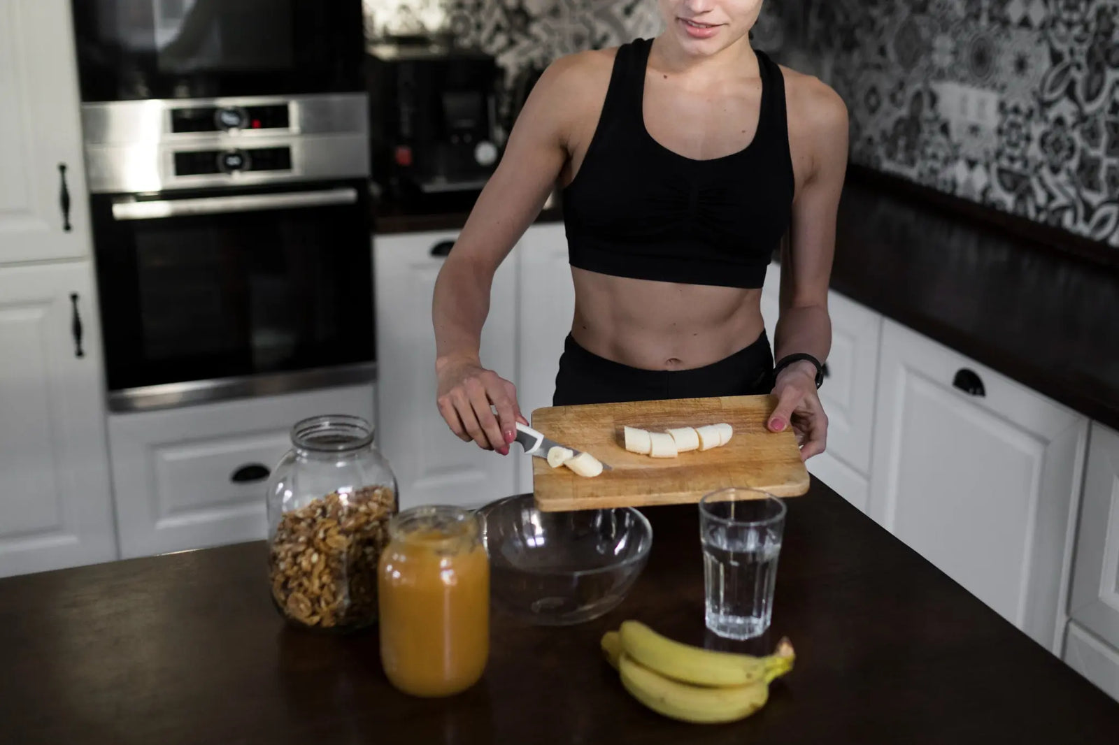 A woman in her workout clothes preparing a healthy meal of chopped banana, peanut butter and walnuts.